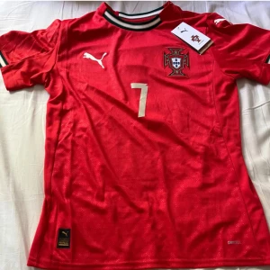 Portugal Ronaldo 7 fotbollströja  - Portugal landslagströja från Puma med Ronaldo och nummer 7 på ryggen. Röd med vita detaljer, broderat landslagsemblem och Puma-logga. Kortärmad modell i lätt och ventilerande material, perfekt för fotboll eller träning.
