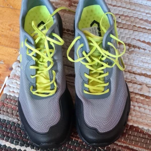 Craft Trail grå/gula löparskor - Snygga trail-löparskor från Craft i grått med svarta detaljer och neon-gula snören och innersula. Ovandelen är i slitstark syntet med mönstrad struktur och sidorna har gula prickar. Grovmönstrad sula för extra grepp på stigar.