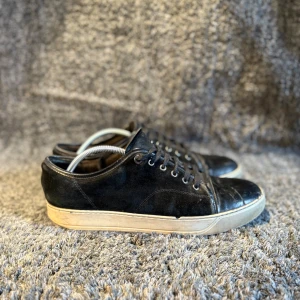 Lanvin skor  - Stilrena svarta sneakers från Lanvin med ovandel i skinn och mocka, rund tå och vita gummisulor. Klassisk design med snörning och diskreta detaljer, perfekt för dig som gillar en clean look med lyxig känsla.