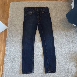 Nudie Jeans Lean Dean mörkblå jeans - Mörkblå Lean Dean jeans från Nudie Jeans i klassisk femficksmodell. Slimmad passform med raka ben och snygga kontrastsömmar. Tillverkade i 99% bomull och 1% elastan för lite stretch. Perfekta för dig som gillar stilrena och bekväma jeans.