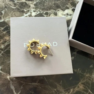 Guldiga örhängen från Edblad - Två par snygga örhängen från Edblad i guldig färg. Ena paret är runda hoops med coola taggiga detaljer, det andra paret är avlånga med geometriskt mönster. Perfekta accessoarer för att lyfta din stil.