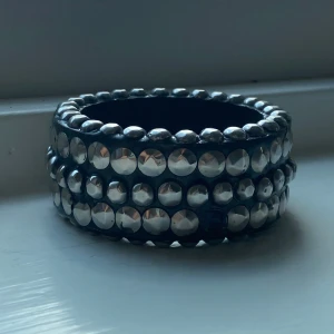 Brett svart armband med silvriga nitar/stenar - Coolt brett armband i svart med silvriga nitar/stenar runt hela. Skit coolt armband som verkligen kan göra en outfit. En av de silvriga nitarna/stenarna har ramlat av men annars är de i toppskick! Köpt från Sellpy men aldrig använt själv då de inte passade. Diamater i cm = 7. Hör av dig om du har några frågor!💞💞