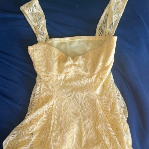 Gul spetsklänning med axelband - Söt gul klänning med breda axelband och spetsmönster. Storken Xs