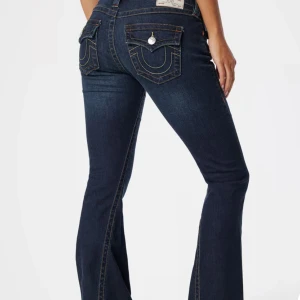 True Religion mörkblå bootcut jeans - Mörkblå jeans från True Religion med bootcut passform och snygga kontrastsömmar. Klassiska fickor bak med ikonisk broderad logga och silverfärgade knappar. Jeansen har låg midja och är tillverkade i stretchig denim för en bekväm känsla.
