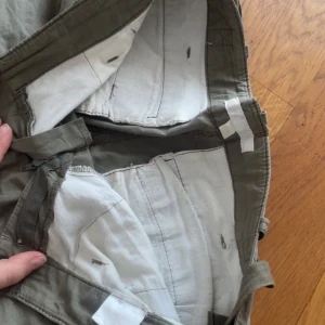 Olivgröna cargobyxor från By de Line - Olivgröna cargobyxor från By de Line med flera stora fickor på benen och klassisk dragkedja. Byxorna har en loose passform och är tillverkade i bomull, perfekta för en avslappnad och cool stil.