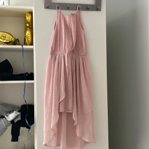 Ljusrosa prickig klänning Lindex 128 - Supersöt ljusrosa klänning från Lindex med tunna axelband och volangdetaljer framtill. Klänningen har ett prickigt mönster och är längre bak än fram, vilket ger en snygg och lekfull look. Perfekt för sommarens alla tillfällen!