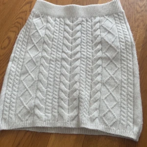 Ljus stickad kjol från Amisu - Supermysig ljusgrå stickad kortkjol från Amisu med snyggt flätmönster och ribbad midja. Perfekt att styla med en oversized tröja och boots för en chill vibe. Kjolen är mjuk och skön, passar både till vardags och när du vill vara extra cozy.