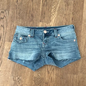 True Religion jeansshorts low rise - Snygga ljusblå jeansshorts från True Religion, modell Joey Cut-Off med låg midja. Klassisk femficksdesign, råa kanter och röda detaljer på bakfickorna. Perfekta för sommaren säljer för använder de inte använd vara 2 gånger köpt för 849