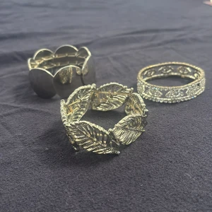 3-pack silvriga armband med olika mönster - Säljer tre snygga armband i silverton: ett med stora blanka cirklar, ett med detaljerade löv och ett glittrigt med stenar och ögonmönster. Perfekt för dig som vill mixa och matcha olika stilar och sticka ut lite extra.