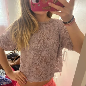 Ljuslila volangblus med 3D-effekt - Superfin ljuslila blus med kort ärm och transparent tyg täckt av 3D-volanger.