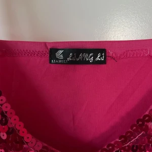 Rosa paljettklänning från Liangli - Supersnygg rosa kortklänning med smala axelband och massor av glittrande paljetter framtill. Klänningen har en figurnära passform och är perfekt för dig som vill sticka ut. Materialet är mjukt och stretchigt för en bekväm känsla hela kvällen.