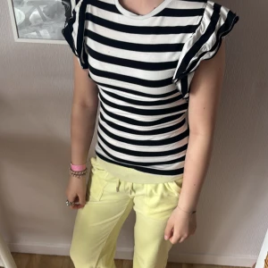 Randig topp med volangärmar - Superfin svartvit randig topp från new yorker med volangdetaljer på ärmarna. Modellen är figurnära och har rund halsringning. Perfekt för dig som gillar en lekfull och trendig stil med extra fokus på axlarna. Aldrig använd!