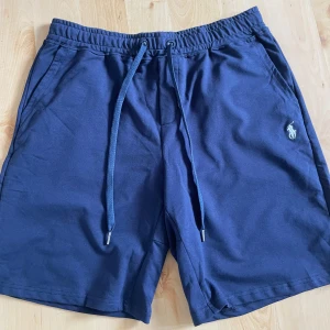 Blå shorts från Polo Ralph Lauren - Marinblå shorts från Polo Ralph Lauren.  Storlek L och passar om man har M eller L. Anledning till att jag säljer är att de var lite stora, fick de i present. Använd ett fåtal gånger utan några som helst anmärkningar. Pris kan diskuteras.