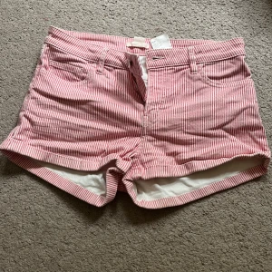 Randiga rosa shorts  - Snygga shorts med smala rosa och vita ränder, klassisk femficksmodell och bälteshällor. De är tillverkade i mjuk bomull och har en avslappnad passform med uppvikta benslut. Perfekta för varma dagar och en chill look.