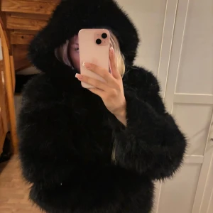 Svart croppad pälsjacka med huva - Säljer en svart, fluffig och croppad pälsjacka med huva. Jackan har långa ärmar och en riktigt mjuk känsla, perfekt för att sticka ut. Stängs med dragkedja framtill och har en oversized vibe. Superfin till kalla dagar när du vill vara extra stylish.
