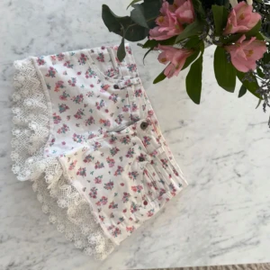 Blommiga vita shorts med spetskant - Säljer för att de inte riktigt är min stil de är typ som nya! Supersöta vita shorts med små rosa och gröna blommor och bred, dekorativ spetskant längst ner. Klassisk femficksmodell med knapp och dragkedja. Perfekta för en somrig look och riktigt gulliga detaljer!