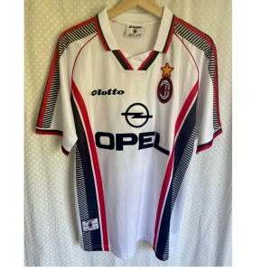 Vintage Jersey AC  Milano  - Klassisk AC Milan bortatröja säsong 1997/1998 med Maldini 3 på ryggen. Tröjan är vit med svarta och röda detaljer, svart OPEL-logga och klubbmärke på bröstet. Snygg krage med röd och svart kant. Tillverkad i lätt polyester, perfekt för samlare eller fans.