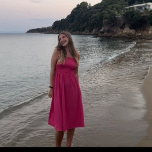 Rosa sommarklänning med smockliv - Säljer en rosa långklänning med smala axelband och smockat liv. Klänningen har en luftig passform och är perfekt för varma dagar. Den är ärmlös och har en enkel, stilren design som ger en fräsch vibe.