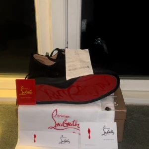 Christian Louboutin svarta sneakers med nitar - Köpta av en polare säljs för jag ej använder dom. Svarta sneakers från Christian Louboutin i mocka med ikonisk röd sula och svarta nitar på tån. Skorna har snörning och en rund tå, vilket ger en edgy och lyxig vibe. Perfekta för dig som vill sticka ut med exklusiva detaljer och streetstyle-känsla. Kvitto finns samt extra nitar om dom skulle falla av alla bitar är på.