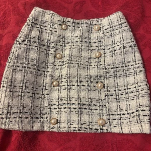 Vit och svart rutig kortkjol med pärlknappar - Superfin kortkjol i vit och svart rutigt tyg med snygga pärlknappar framtill. 