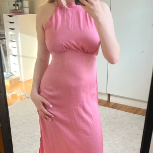 Rosa långklänning från Zara - Supersnygg rosa långklänning från Zara i glansigt material. Klänningen har hög halsringning, är ärmlös och har en slits på sidan. Sitter figurnära upptill och faller snyggt längs kroppen. 