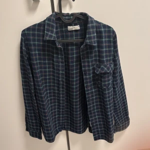 Mörkblå rutig skjorta med ficka - Snygg mörkblå rutig skjorta från Moda med gröna och röda detaljer. Skjortan har klassisk krage, knäppning framtill och en bröstficka med lock. Perfekt att bära öppen över en t-shirt eller knäppt. Långärmad och i mjuk bomull.