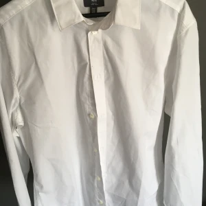 Vit slim fit skjorta från H&M - Klassisk vit skjorta från H&M i slim fit-modell. Skjortan har långa ärmar, knappar framtill och en stilren krage. Tillverkad i bomull och enkel att stryka. Perfekt för dig som gillar en clean och snygg look.