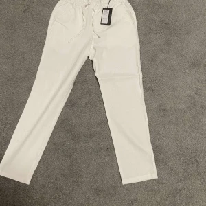 Vita linnebyxor med snörning - Snygga vita linnebyxor med elastisk midja och snörning framtill. Byxorna har raka ben och sidfickor, perfekta för en chill och stilren look. Lätta och luftiga, passar grymt till sommaren.