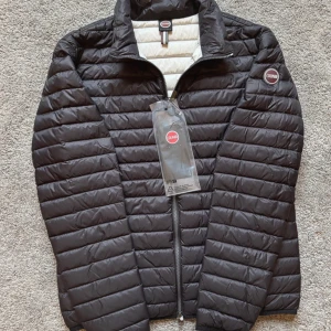 Svart dunjacka från Colmar - Säljer en stilren svart dunjacka från Colmar. Jackan har en quiltad design med dragkedja framtill och en diskret logotyp på bröstet. Perfekt för kyligare dagar med sin lätta och värmande konstruktion.