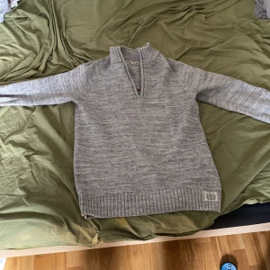 Grå stickad tröja från L.O.G.G. - Säljer en stilren grå stickad tröja från L.O.G.G. med dragkedja vid halsen. Tröjan har långa ärmar och ribbstickade muddar vid ärmslut och nederkant. Perfekt för kyligare dagar.