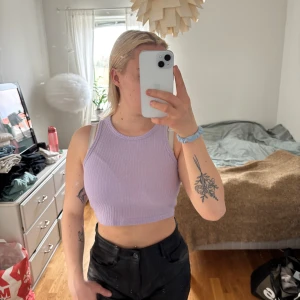 Lila ribbad linnetopp - Säljer en snygg lila ribbad linnetopp. Den är ärmlös och croppad, perfekt för varma dagar. Toppen har en enkel och stilren design som passar till många olika outfits.