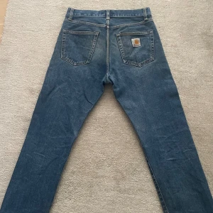 Blå jeans från Carhartt - Säljer ett par klassiska jeans från Carhartt i en ovanlig blå färg med rak passform och den klassiska carhart loggan insydd på bakfickan. De har en knapp och dragkedja framtill samt fem fickor. De har en riktigt skön fadead färg som kommit med tiden vilket gör dem perfekta för en avslappnad stil. De har storlek 29/32 men är större i midjan så skulle passa upp till 30/32