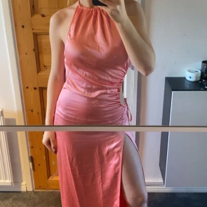 Rosa satinklänning/balklänning - Snygg rosa axelbandslös klänning med hög slits och öppen rygg från NA-KD. Klänningen har en knytning i sidan som ger en fin detalj och är tillverkad i ett glansigt material. Aldrig använd endast testad. Perfekt för balen till sommaren! Kontakta för mer bilder eller frågor 🌸☺️