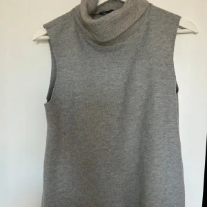 Grå ärmlös polotröja från Zara - Säljer en stilren grå ärmlös polotröja från Zara. Perfekt för lager-på-lager eller som den är. Tröjan har en hög polokrage och är tillverkad i ett mjukt material som ger en bekväm passform.