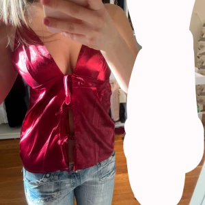 Röd satinlinne med knytning - Snygg röd satinlinne med justerbara axelband och knytning framtill. Perfekt för en kväll ute eller en speciell tillställning. Linnet har en glansig finish som ger en lyxig känsla. 