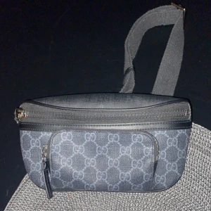 Svart och grå axel/midjeväska med mönster - Snygg axel/midjeväska i svart och grått perfekt för sommaren med ett stilrent mönster. Väskan har en justerbar rem och dragkedja för säker förvaring. Perfekt för att bära med sig det viktigaste på ett smidigt sätt. Pris kan DISKUTERAS 