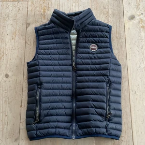 Mörkblå dunväst från Colmar - Säljer en snygg mörkblå dunväst från Colmar. Västen har en dragkedja framtill och två praktiska fickor med dragkedjor. Perfekt för lager-på-lager under kyliga dagar. Märkeslogga på bröstet ger en stilren touch. Modellen är 164 och västen är lite för liten så den borde sitta perfekt om du är runt 158. Skick 10/10