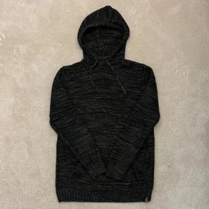 Svart stickad hoodie - Säljer en svart stickad hoodie med en mysig känsla. Den har en praktisk ficka framtill och justerbar huva med snören. Perfekt för kyliga dagar.