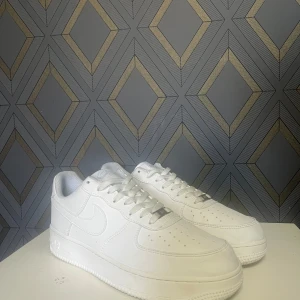 Vita Nike Air Force sneakers - Säljer ett par klassiska vita Nike Air Force 1 ,07 med blanck yta. Använda fåtals gånger men lite creasede De har en stilren design med snörning och rund tå. Perfekta för en casual look och passar till det mesta i garderoben.