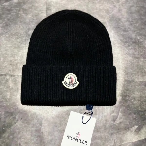Svart Moncler mössa - Helt ny och aldrig använd svart Moncler-mössa. Perfekt skick och redo för användning. Skriv om ni har frågor eller funderingar! 😊