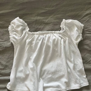 Vit topp från Gina Tricot - Säljer en söt vit topp från Gina Tricot med puffiga korta ärmar och elastisk halsringning.