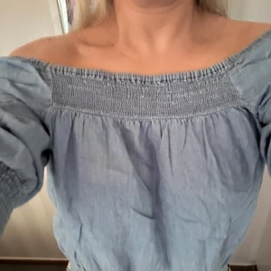 Blå offshoulder topp från H&M - Säljer en snygg blå offshoulder topp från H&M. Toppen har trekvartsärmar och en elastisk smockdetalj vid halsringningen och ärmsluten. Perfekt för en avslappnad stil.