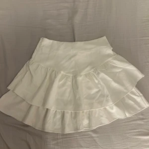 Vit volangkjol - Snygg vit kortkjol med volanger, har dragkedja på sidan. 