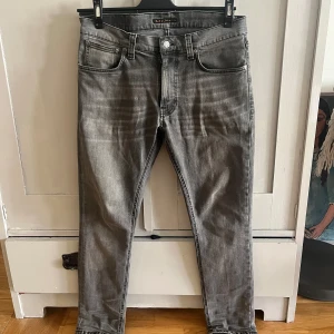 Grå jeans från Nudie Jeans - Snygga grå jeans från Nudie Jeans med en klassisk femficksdesign. De har en normal passform och är tillverkade i slitstarkt denim. Perfekta för en stilren look. Modellen är lean Dean och storlek 31w 30L