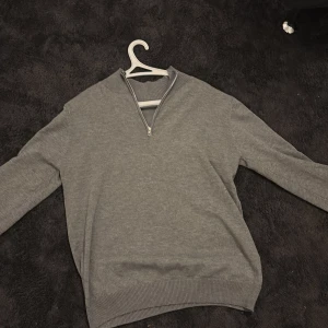 Grå tröja med half zip  - Säljer en stilren grå tröja med dragkedja vid halsen. Tröjan har långa ärmar och ribbade muddar vid ärmslut och nederkant. Perfekt för en avslappnad look. Aldrig använd!!