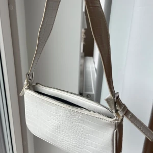 Vit väska med krokodilmönster - Snygg vit axelväska från Ginatricot med krokodilmönster och dragkedja. Perfekt för att ge en stilren touch till din outfit. Väskan har en justerbar rem och ett rymligt fack.