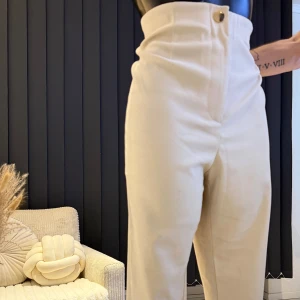 Vita högmidjade byxor - Snygga vita byxor med hög midja och knappdetalj. Perfekta för en stilren look. Byxorna har en rak passform och är tillverkade i ett mjukt material som ger en bekväm känsla. Jättefina och moderna byxor från Zara butik. Passar perfekt i M/L storlek.🌸👌