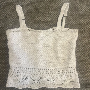 Vit broderad topp från Hollister - Säljer en söt vit broderad stickad topp från Hollister med justerbara axelband. Toppen har ett vackert spetsmönster längst ner och är perfekt för sommardagar 💕🌷 