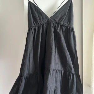 Svart klänning från Zara - Snygg svart klänning från Zara med smala axelband och v-ringad design. Klänningen har en luftig passform och volangdetaljer som ger en fin rörelse. Perfekt för en stilren look.