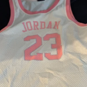 Vit och rosa basketlinne från Air Jordan - Säljer ett gult basketlinne från Air Jordan med rosa detaljer och nummer 23 på framsidan. Linnet har en lös passform och är perfekt för sportiga aktiviteter. Tillverkad i ett lätt och luftigt material. Endast använt en gång inga märken 